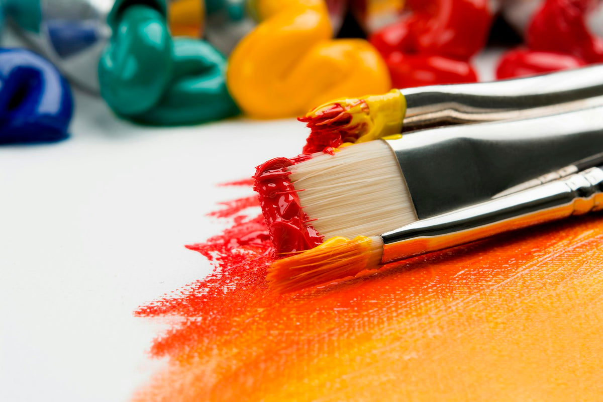 Acrylic paints, brushes and a canvas laid out on a wooden table