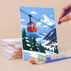 Painting an Alpine Ski Days mini canvas propped up beside numbered acrylic paints