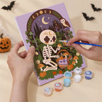 Hand holding a Boho Skeleton Hideaways mini canvas while painting the details