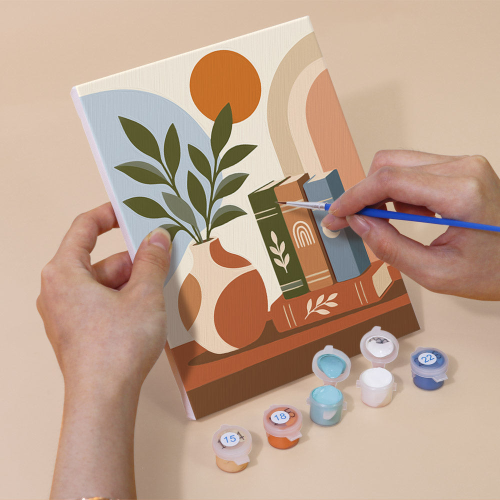 Hand holding a Book Lover's Corner mini canvas while painting the details