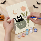 Hand holding a Botanical Black Cats mini canvas while painting the details