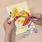 Hand holding a Breakfast Spread mini canvas while painting the details