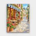 Cafe on the Hill paint by numbers kit of a cafe with striped awnings, red geraniums and bistro tables along a winding cobbled street