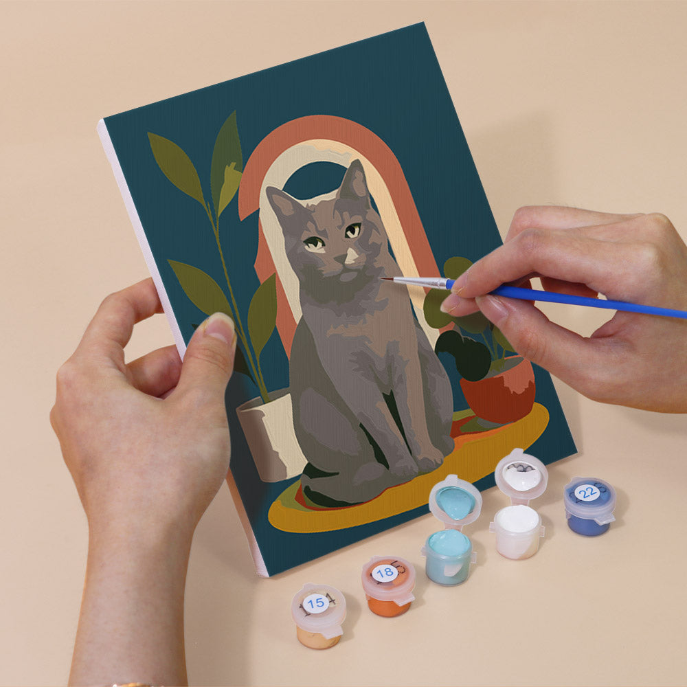 Hand holding a Cats Through the Seasons mini canvas while painting the details
