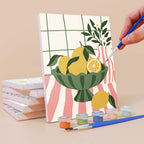 Painting a Checkerboard Still Life mini canvas propped up beside numbered acrylic paints