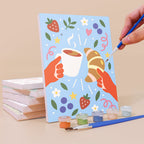 Painting a Cheers and Treats mini canvas propped up beside numbered acrylic paints