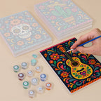 Painting one of the Día de Muertos designs next to a stack of mini canvases