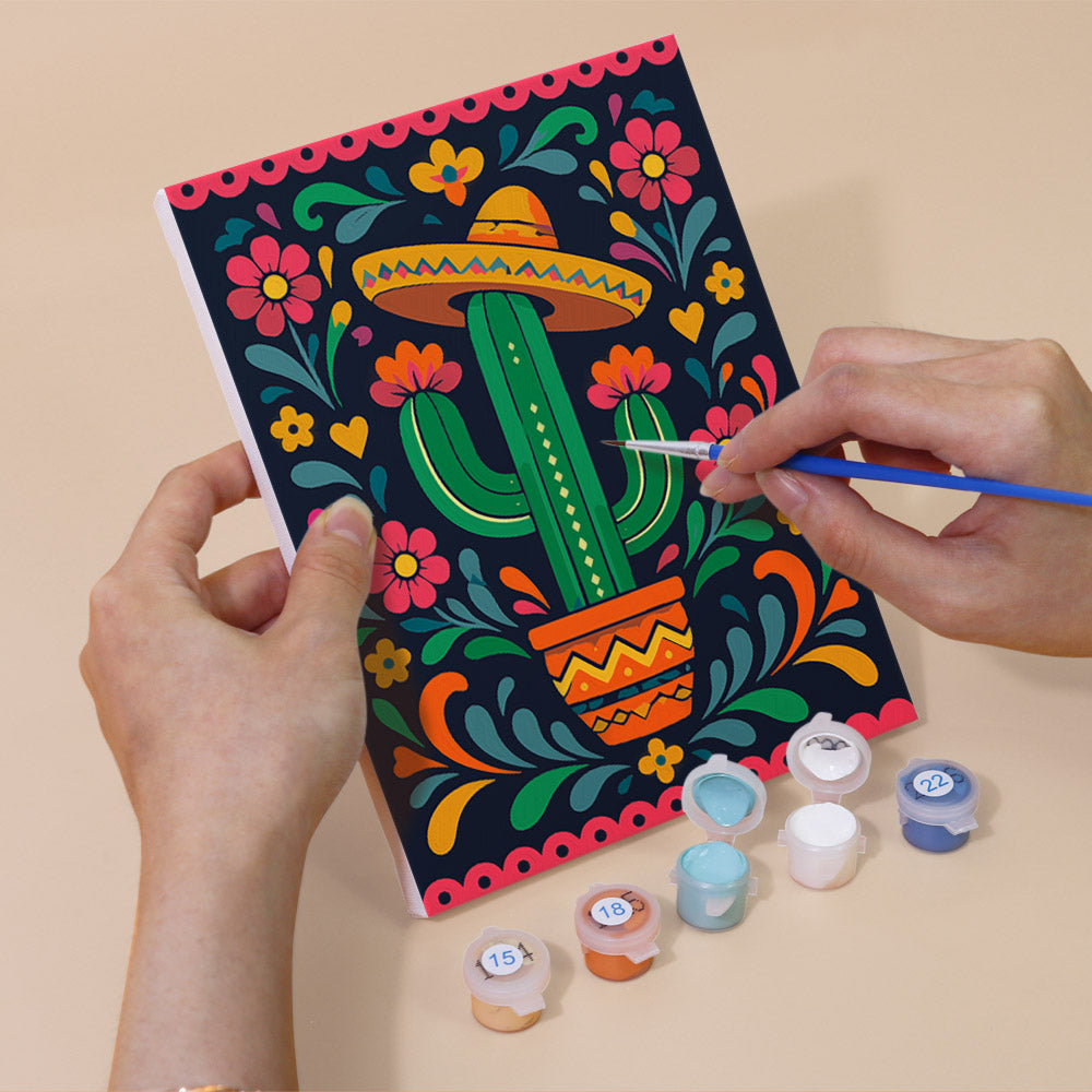 Hand holding a Día de Muertos mini canvas while painting the details
