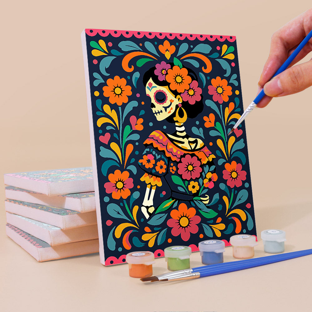 Painting a Día de Muertos mini canvas propped up beside numbered acrylic paints