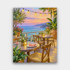 Dinner by the Sea paint by numbers kit of a seaside restaurant deck with string lights, candlelit tables and a pink dusk sky