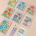 Folk Flower Tiles mini paint by numbers set: six folk-art flower canvases with wavy borders laid out with numbered paint pots, three brushes and the reference layout