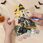 Hand holding a Haunted Pumpkin Cottages mini canvas while painting the details