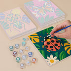 Painting one of the Jungle Bugs designs next to a stack of mini canvases