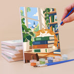Painting a Library Hours mini canvas propped up beside numbered acrylic paints