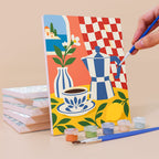 Painting a Majolica Summer mini canvas propped up beside numbered acrylic paints
