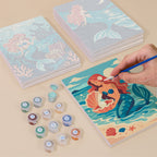 Painting one of the Mermaid Tales designs next to a stack of mini canvases