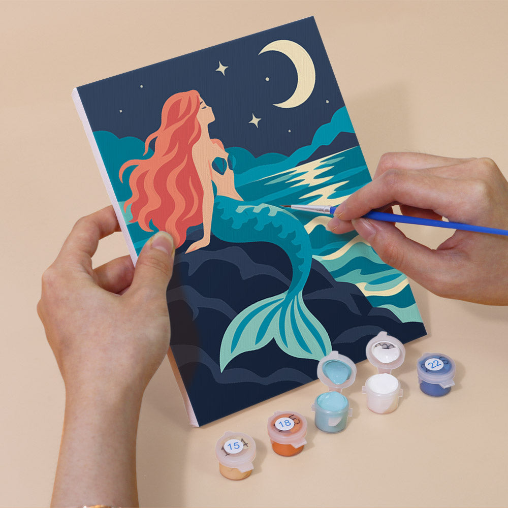 Hand holding a Mermaid Tales mini canvas while painting the details