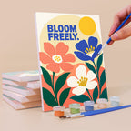 Painting a Mindful Mantras mini canvas propped up beside numbered acrylic paints