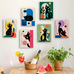 Six finished Mod Cats mini paintings hung on a wall above a table