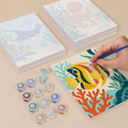 Painting one of the Ocean Friends designs next to a stack of mini canvases