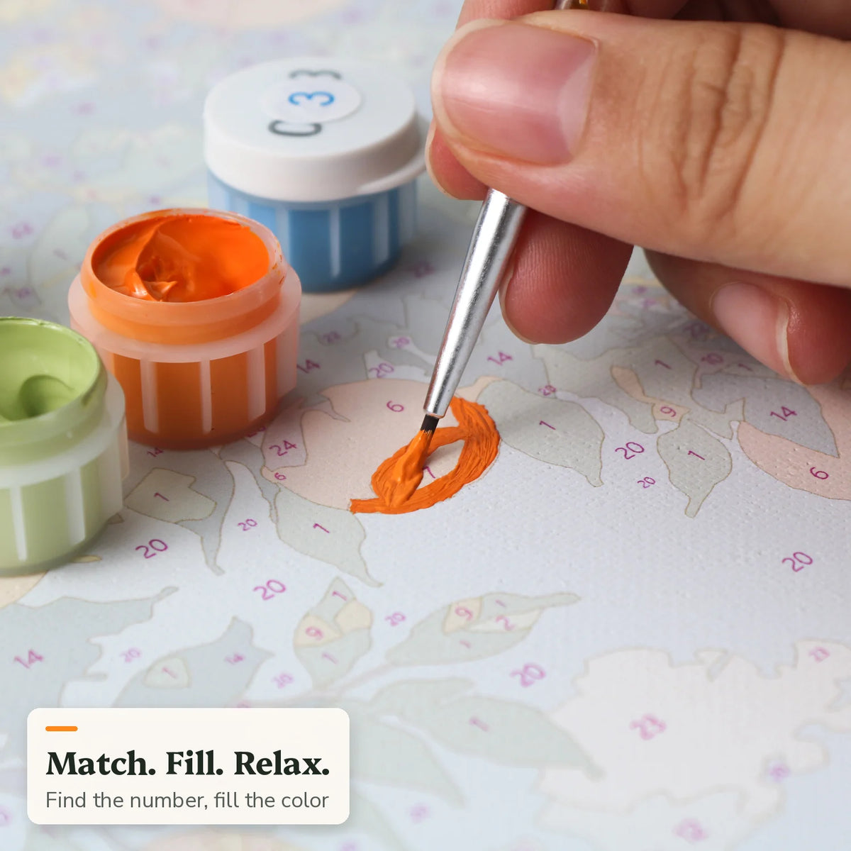 Brush filling a numbered area with orange paint on a paint by numbers canvas