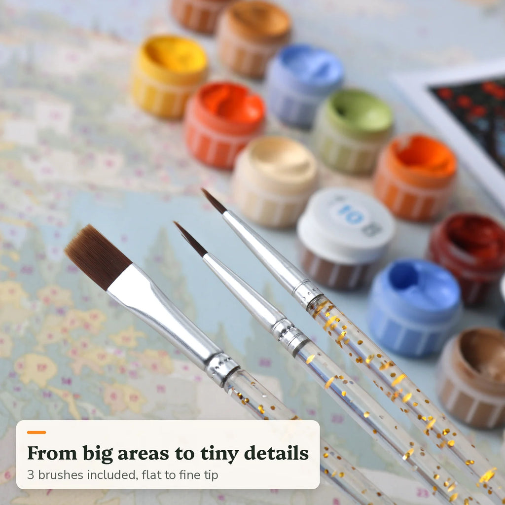 Three paint by numbers brushes, from flat to fine tip, next to acrylic paint pots
