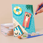 Painting a Palm Beach Holiday mini canvas propped up beside numbered acrylic paints