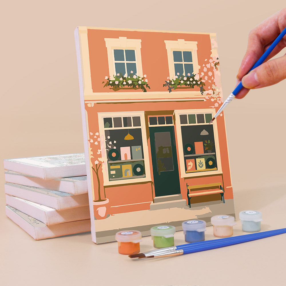 Painting a Pastel Storefronts mini canvas propped up beside numbered acrylic paints