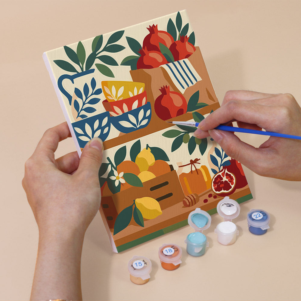 Hand holding a Pomegranate Kitchen mini canvas while painting the details