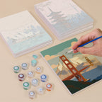 Painting one of the Postcards from Afar designs next to a stack of mini canvases