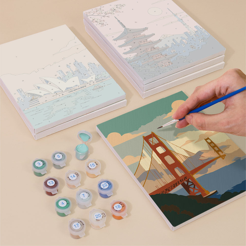 Painting one of the Postcards from Afar designs next to a stack of mini canvases