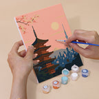 Hand holding a Postcards from Afar mini canvas while painting the details