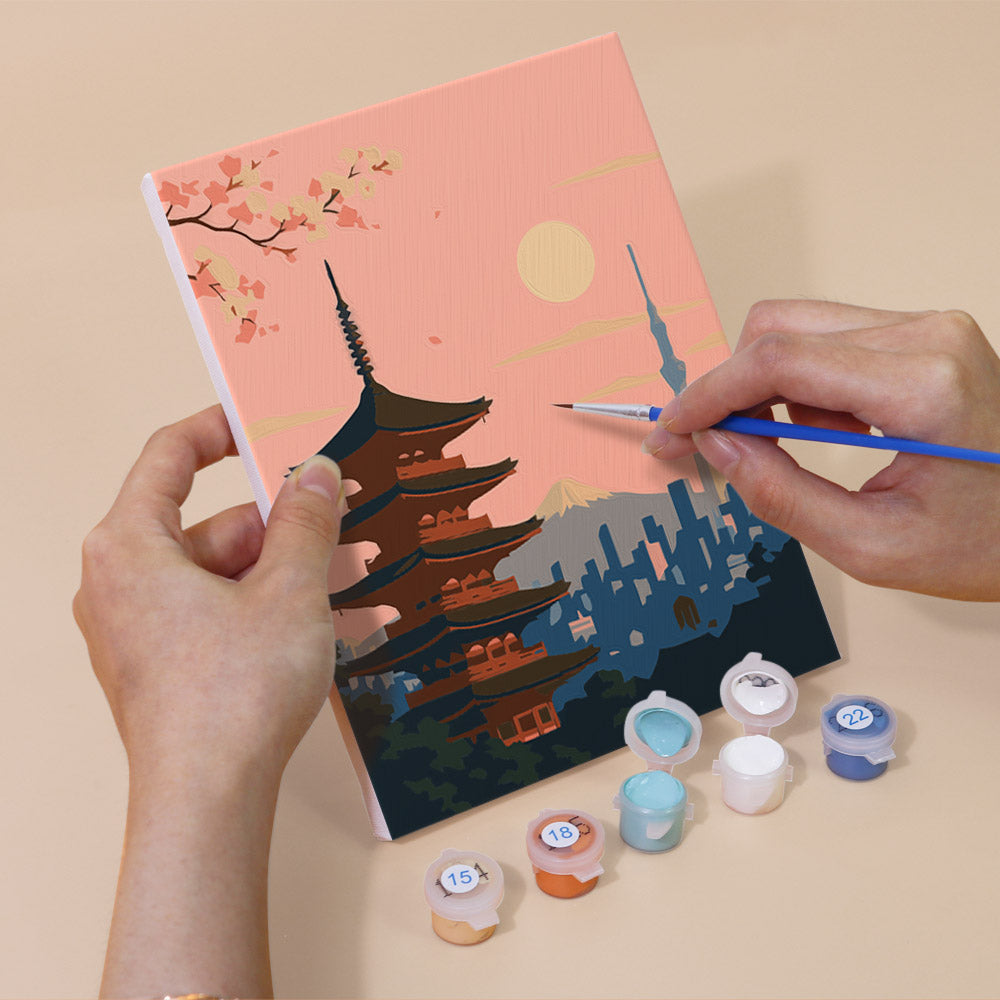 Hand holding a Postcards from Afar mini canvas while painting the details