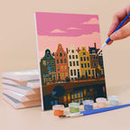 Painting a Postcards from Afar mini canvas propped up beside numbered acrylic paints