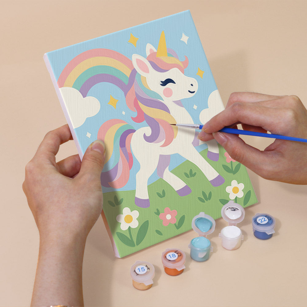 Hand holding a Rainbow Unicorns mini canvas while painting the details