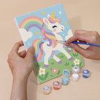 Hand holding a Rainbow Unicorns mini canvas while painting the details