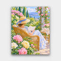 Reading in the Garden paint by numbers kit of a woman in a straw hat reading in a wicker chair in a flowering summer garden