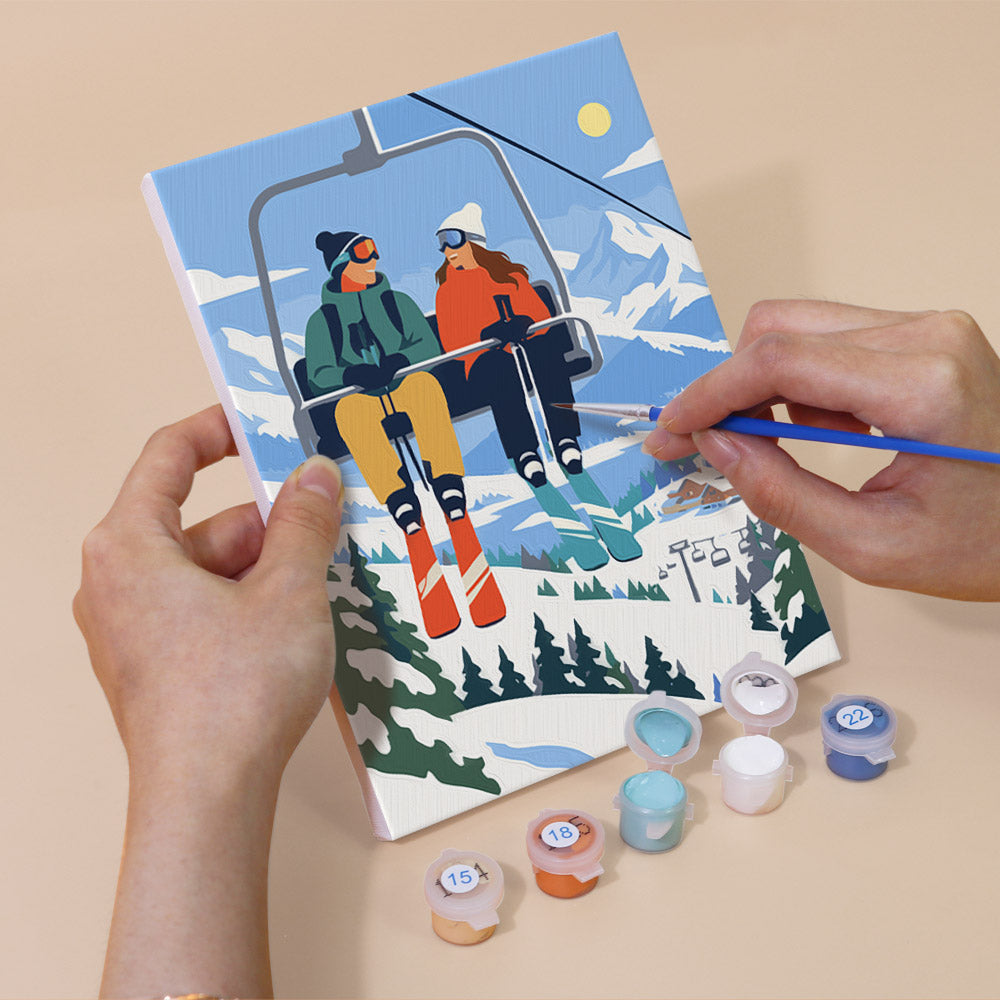 Hand holding a Snow Day Skiers mini canvas while painting the details