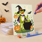 Painting a Spooky Frog Masquerade mini canvas propped up beside numbered acrylic paints