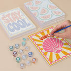 Painting one of the Stay Cool Summer designs next to a stack of mini canvases