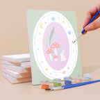 Painting a Storybook Cameos mini canvas propped up beside numbered acrylic paints