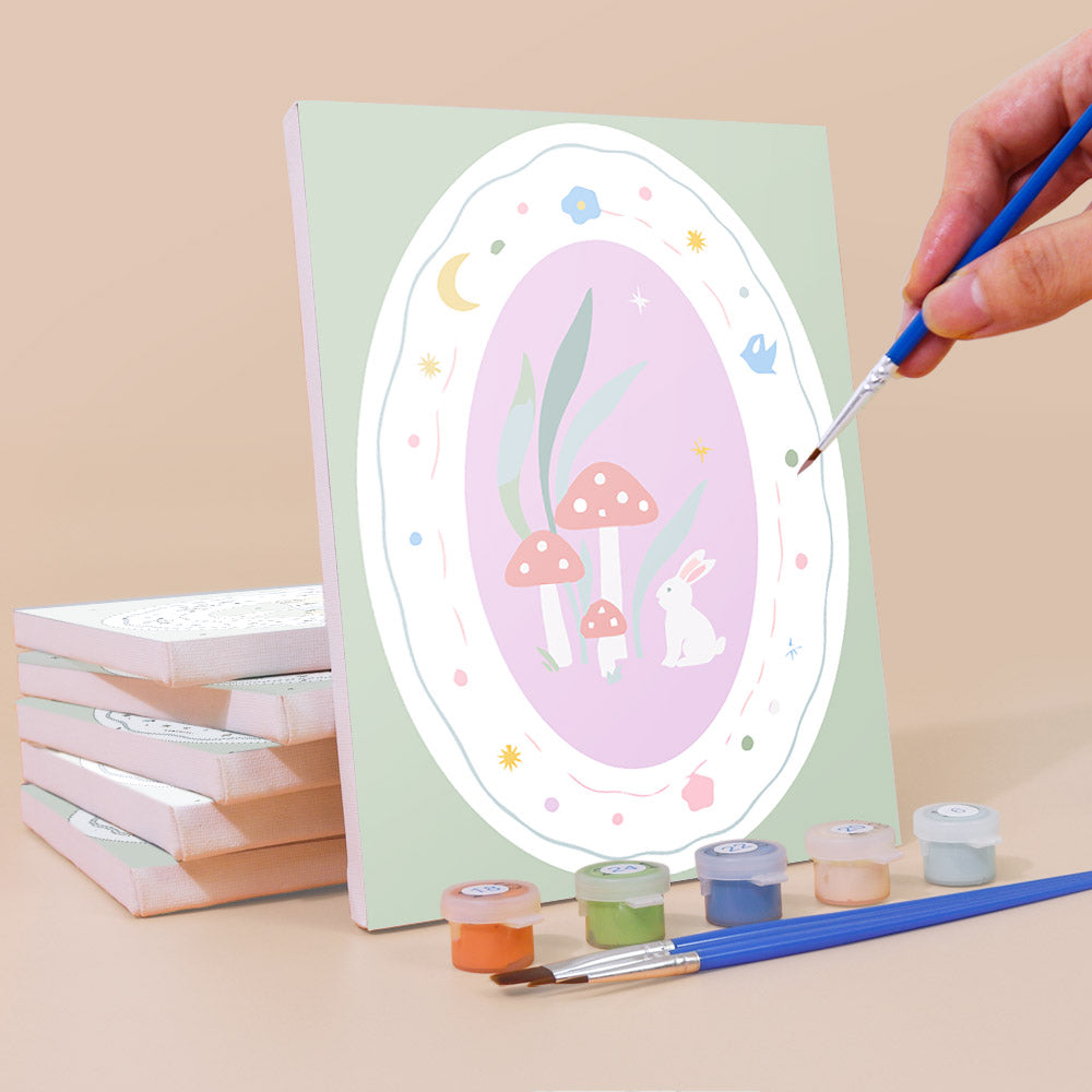 Painting a Storybook Cameos mini canvas propped up beside numbered acrylic paints