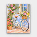 The Blue Bicycle paint by numbers kit of a pale blue bicycle with a wicker basket of wildflowers against a wall of climbing roses