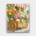 The Flower Cart paint by numbers kit of a wooden cart loaded with buckets of tulips, roses and daisies on a cobbled street