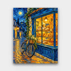 The Night Bakery paint by numbers kit of a glowing bakery window full of bread and pastries on a cobbled street at night
