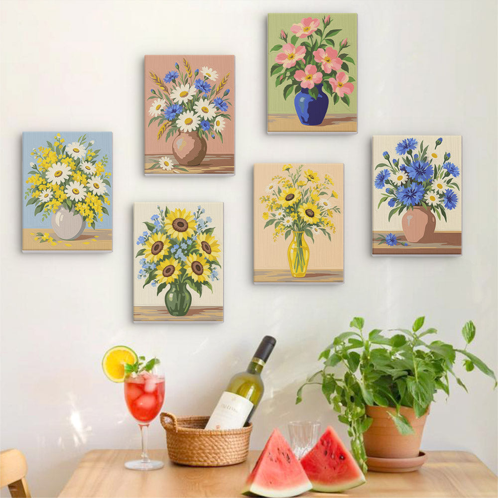 Six finished Wildflower Vases mini paintings hung on a wall above a table
